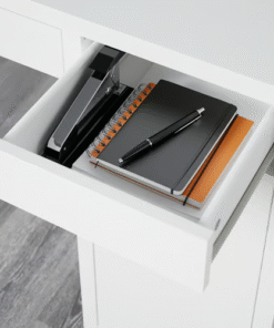 Open drawer of a white desk showing notebooks and stationery inside